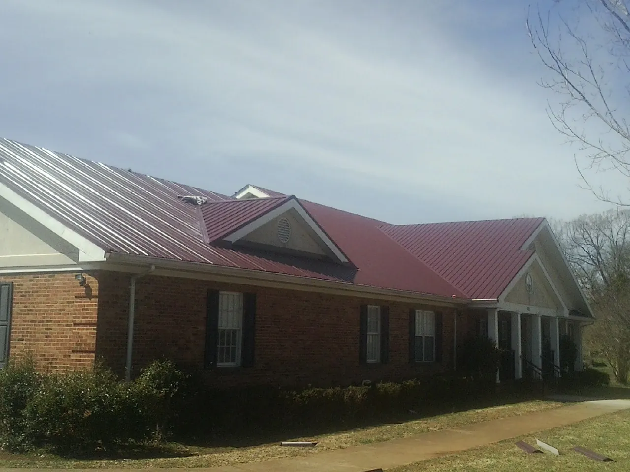 Red metal roof with gabled entries on a long brick building, from a Hail Damage Roof Repair job in Shartlesville