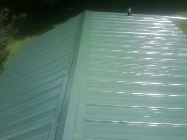 New green metal panels meeting at the ridge of a roof — Flat Roof Repair work by our crew in Shartlesville
