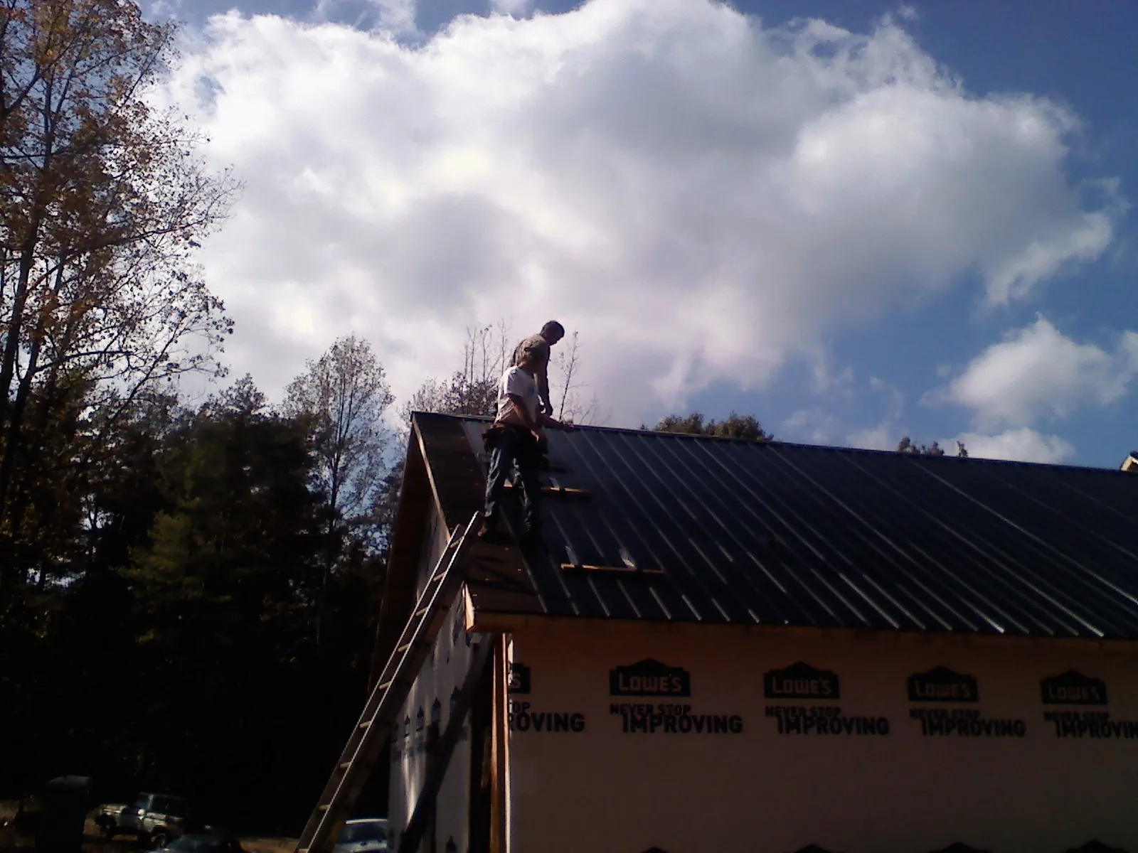 Roofer fastening dark metal panels high against a cloudy sky, from a Roof Inspection job in Shartlesville