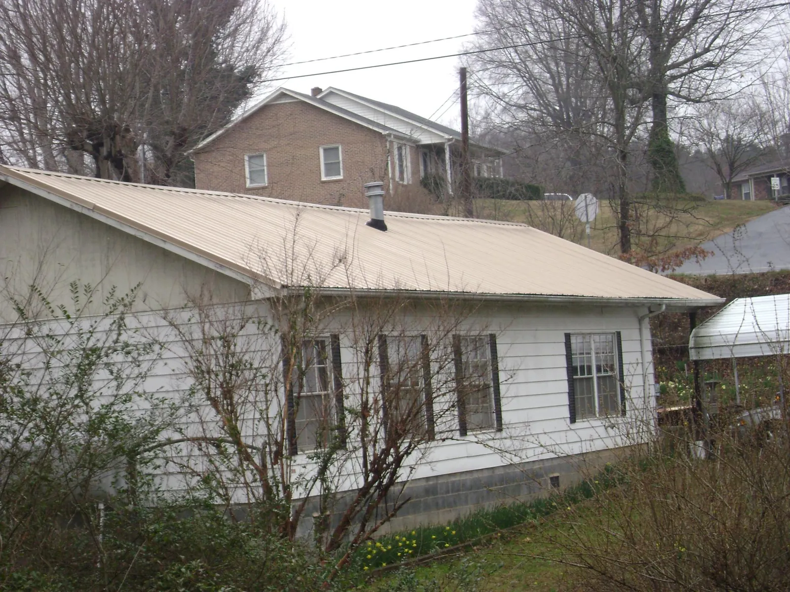 Tan metal roof on a white sided house set into a hillside — Commercial Roofing by Roofing Brothers in Shartlesville
